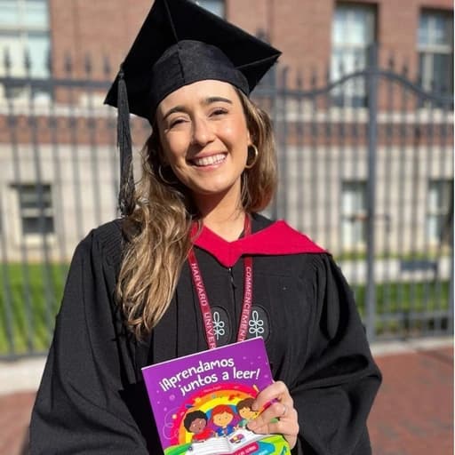 Agustina Ollivier con toga de graduación en Harvard, sosteniendo Aprendamos juntos a leer